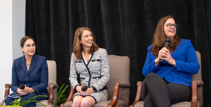 President Cowley smiles with two other panelists on stage while holding the mic.