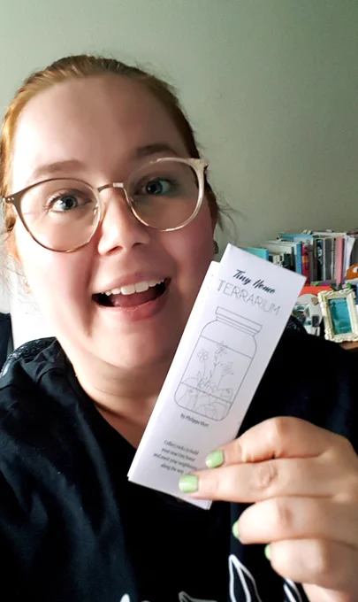 Photo of Philippa, a fat smiling ginger lady, holding a physical copy of the tri-folded zinne Tiny Home Terrarium.