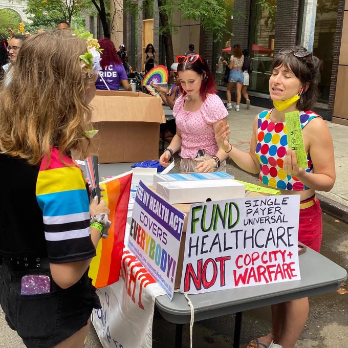 People talking over a table with colorful signs & flyers for the ny health act