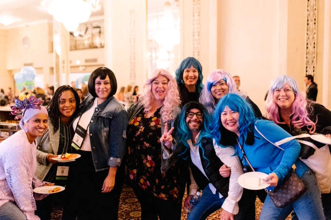 Nine people smile at the WIDA reception. Some of them wear blue or pink wigs