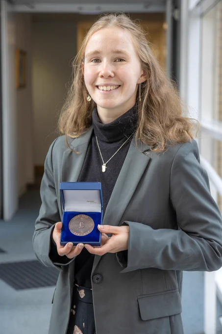 Sophie Young in formal attire smiling and holding a medal in a blue medal case. 