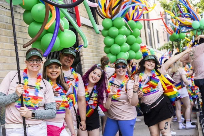 Group of Rush staff members smiling and wearing colorful attire at the Chicago Pride parade, surrounded by vibrant balloons and rainbow flags.