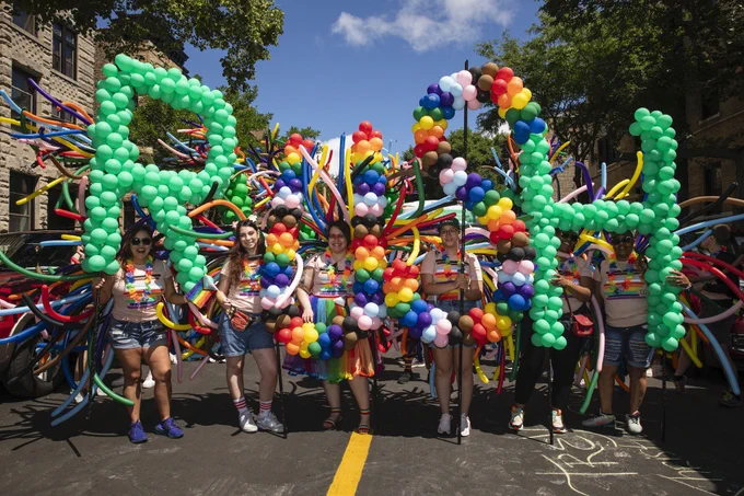 Group of Rush staff members participating in the Chicago Pride parade, adorned with vibrant balloons. The scene features a sunny day with some buildings and trees in the background.