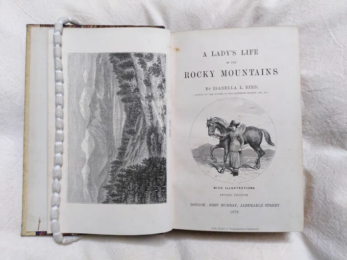 The front page of a book entitled 'A Lady's Life in the Rocky Mountains', with a picture of a lady and horse, resting on a book pillow. 