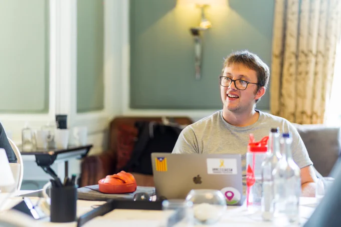 A photo of Bobbie wearing a grey sweater in front of a laptop smiling. 