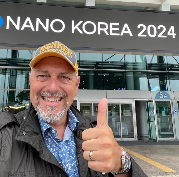 NanoWorld AG AFM probes CEO Manfred Detterbeck in front of the KINTEX building in Soth Korea which is currently showing the signage for this week's Nano Korea 2024 exhibition and conference. He is smiling and showing a "thumbs-up" for the success of the upcoming conference and exhibition.