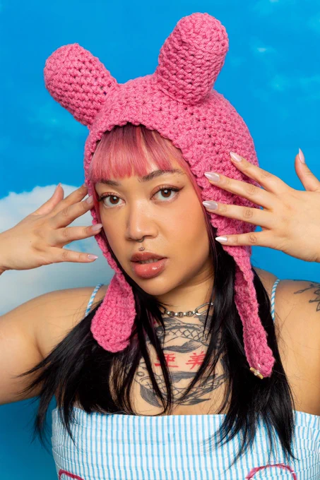 Woman wearing pink bunny ears, with black hair. Her hands are raised to her face and she looks quite serious.