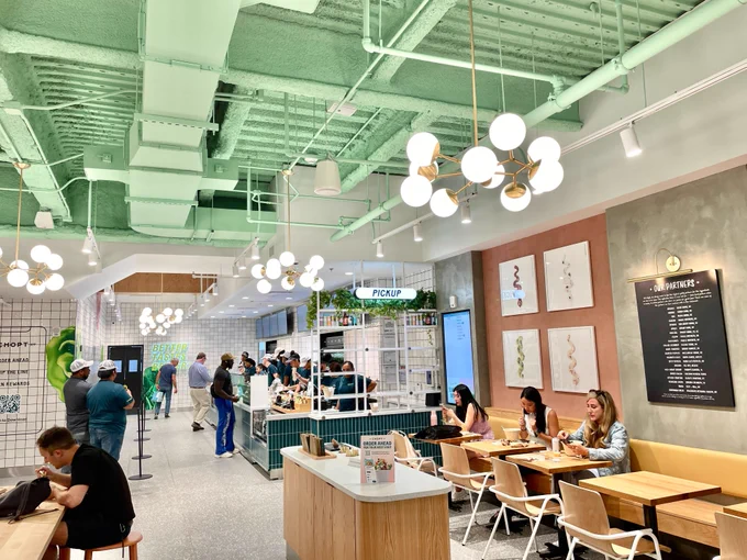The green interior of Chopt, with customers seated and dining inside, and others waiting in line and ordering their food.