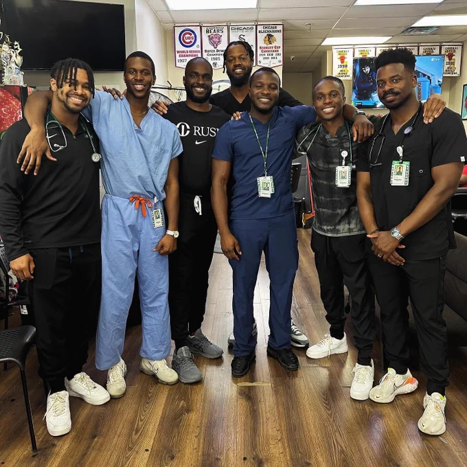 Seven Rush Medical College students posing together in a barber shop at a community event. All are standing and smiling towards the camera.