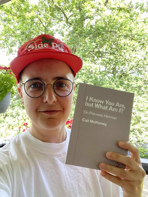 Cait McKinney posted outdoods in the sun holding a copy of the book I Know You Are but What Am I?