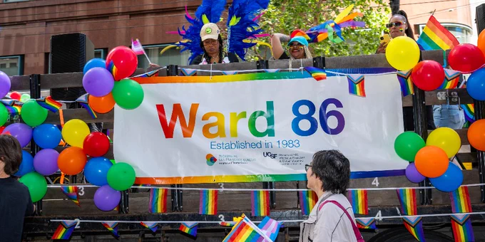 Individuals celebrate on a float decorated with colorful balloons and a banner reading "Ward 86, Established in 1983" during a pride parade.
