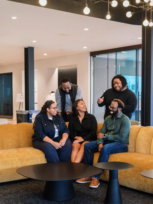 Black Code Collective organizers sitting on a yellow couch in the middle of an office, laughing and joking