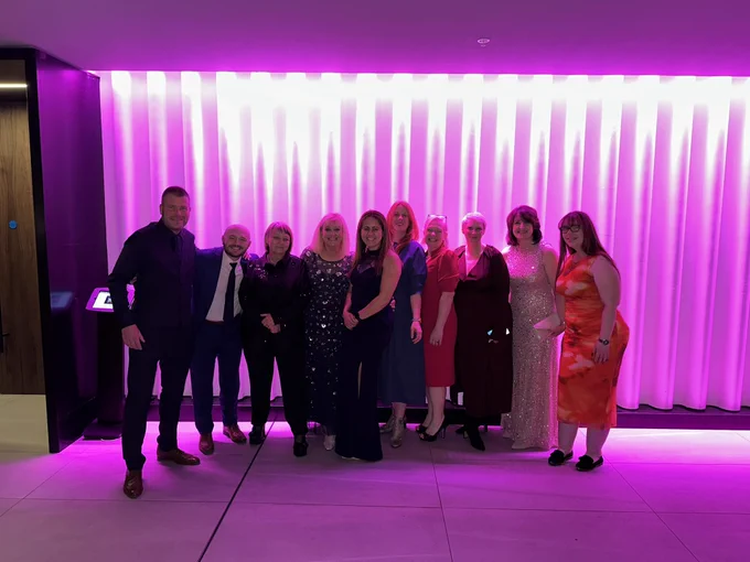 Ten people in front of a pink light background.