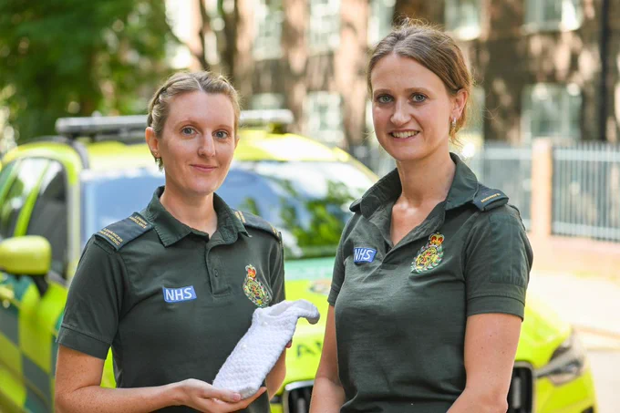 Image shows Advanced Paramedic Nicola, and Lead Midwife Camella with a cuddle pocket, in front of an LAS fast-response car. 