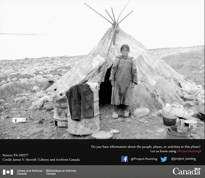 A woman standing on rocky ground outside a tent made of animal skins.