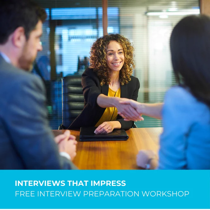 A smiling woman in an interview shakes hands with another woman across a table with a man beside her. 