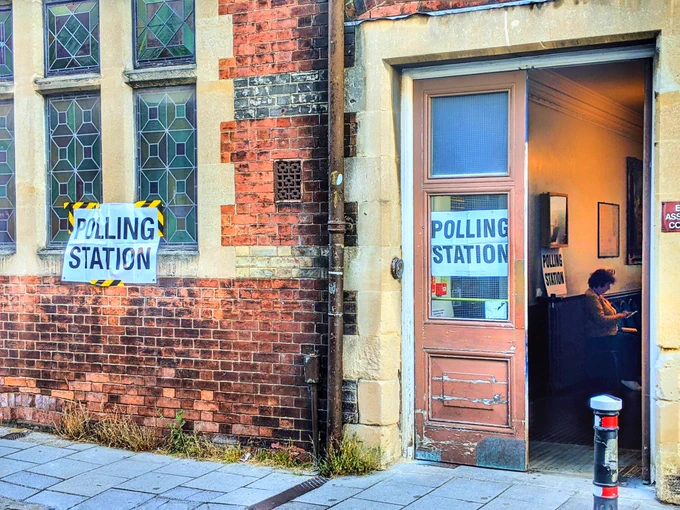 A polling station in a 19th century town hall. A teller is visible inside.