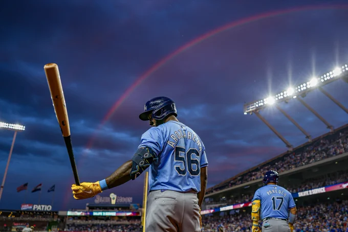 A low-angle shot of Randy Arozarena standing in the on-deck circle as a rainbow spans the sunset sky above Kauffman Stadium. (Photo: Sydney Schneider/Major League Baseball)