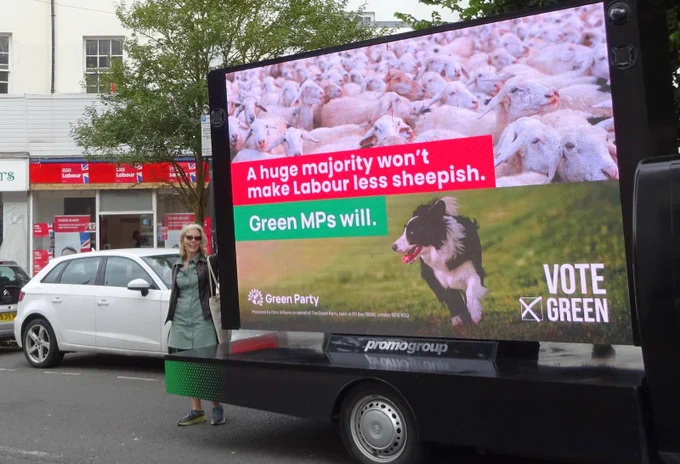 Brighton Kemptown and Peacehaven Green Party election candidate 2024 Elaine Hills outside Brighton Labour’s new office in Kemptown. She is standing next to the Green Party’s ad van on which a billboard states: A huge majority won’t make Labour less sheepish. Green MPs will.