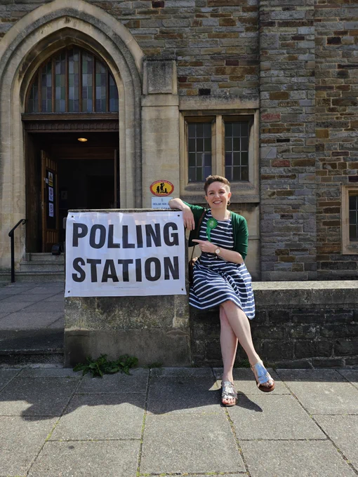 Carla outside a polling station sign in front of a church in the sun and smiling! 