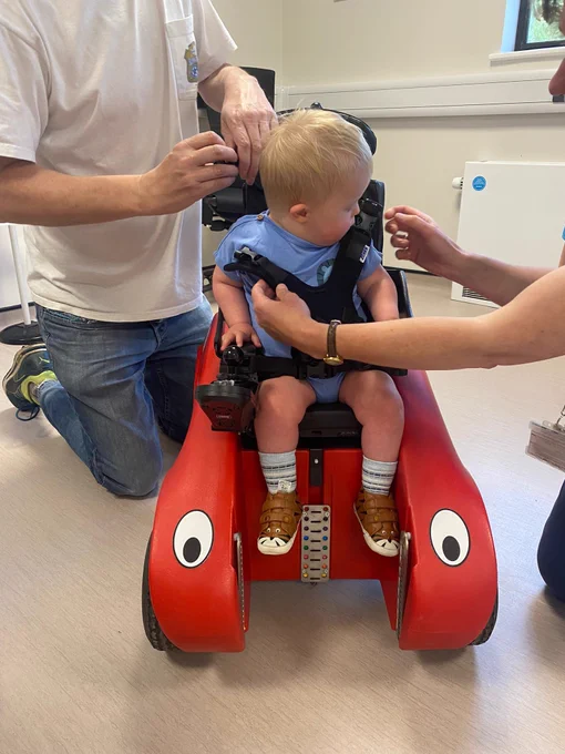 Morris looking at the harness being added across him on his Wizzybug powered wheelchair