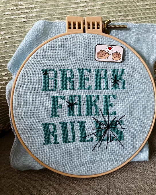 Cross stitch piece of blocky text “break fake rules” with glass cracks running through