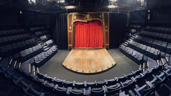 A photo of a red and gold set, with a red curtain and seats curving all around