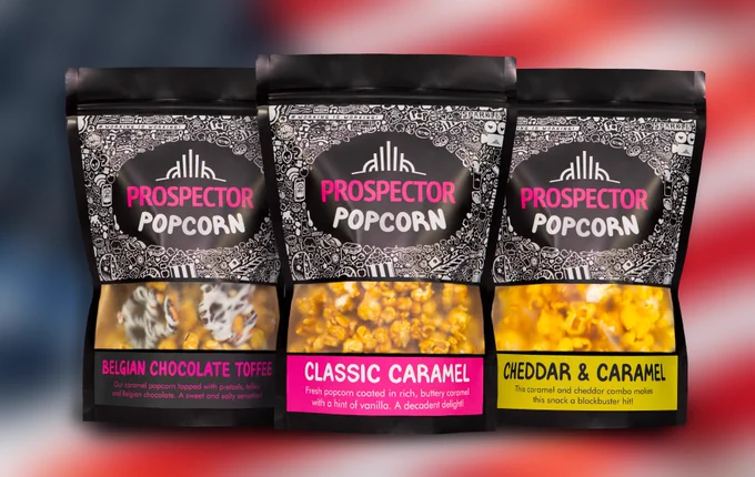 Three bags of gourmet popcorn sit on top of a blurry American Flag.