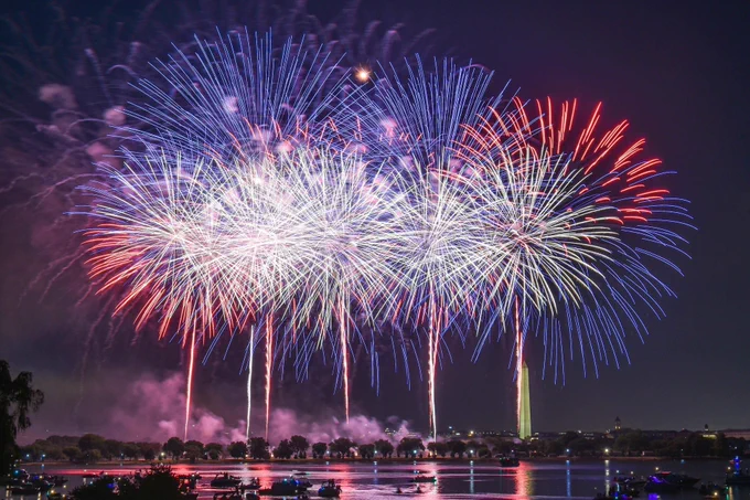 Red, white, and blue fireworks exploding in the night sky over the Washington Munument.