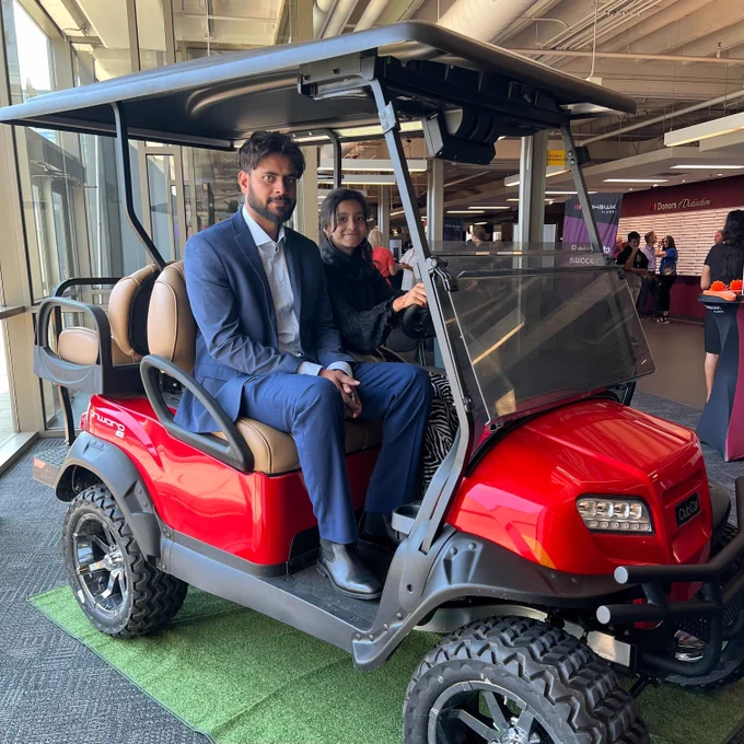 Two people sitting on a golf cart smiling at the camera.