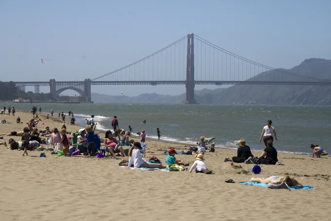 A photo of people on a beach with the golden gate bridge in background