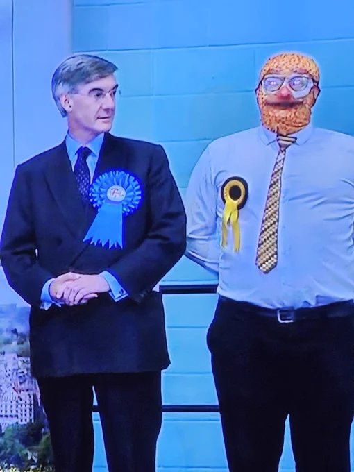 A man from the actual Victorian era stands befuddledly next to the love child of Mr Blobby and a full English. This is genuinely how British elections look, and I couldn't love it more