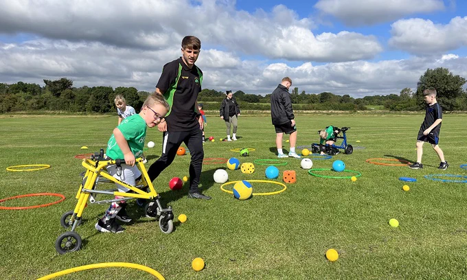 Football coach on outdoor pitch guiding young children 