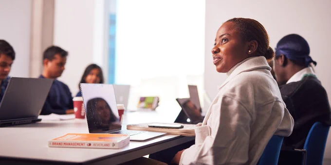 A student listens attentively during a university class, as other students work on their laptops.