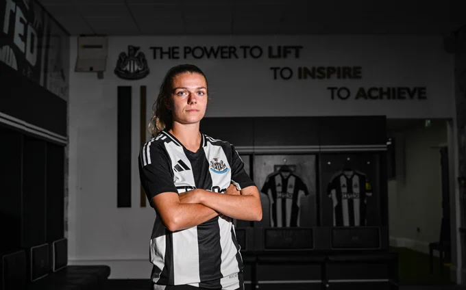 Andrews stands in front of the "Power to lift, to inspire, to achieve" quote in the changing room.