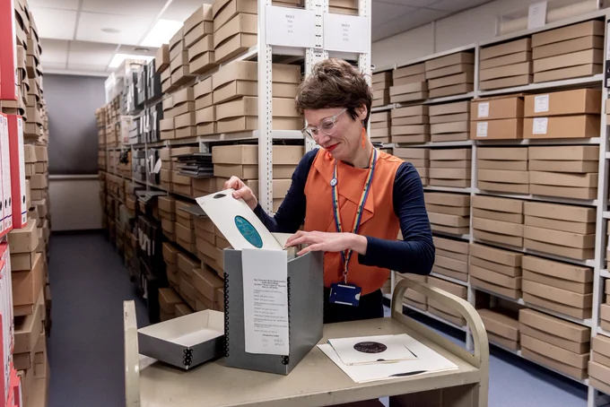 An archivist removing a record from a box in a repository