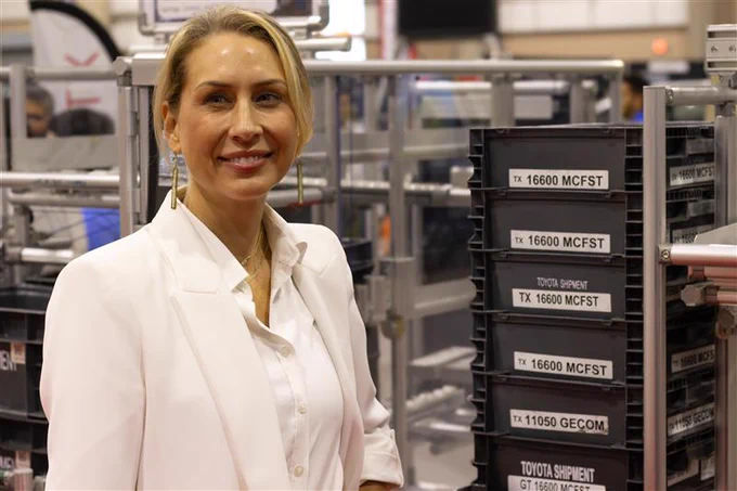 A person smiling at a logistics warehouse, standing in front of shelves filled with labeled containers.