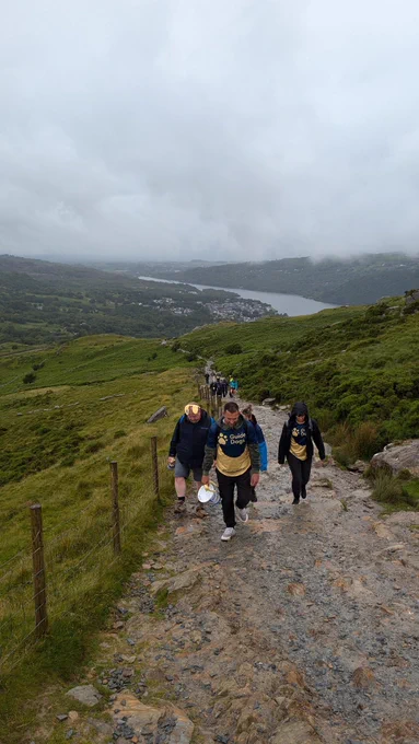 Group of Guide Dogs volunteers hiking up a mountain path with a lake in the distance 