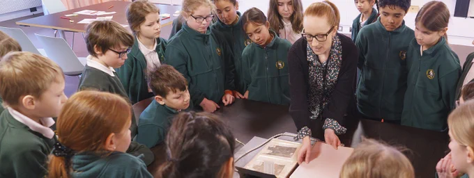 Students stand around a teacher who shows them a document.