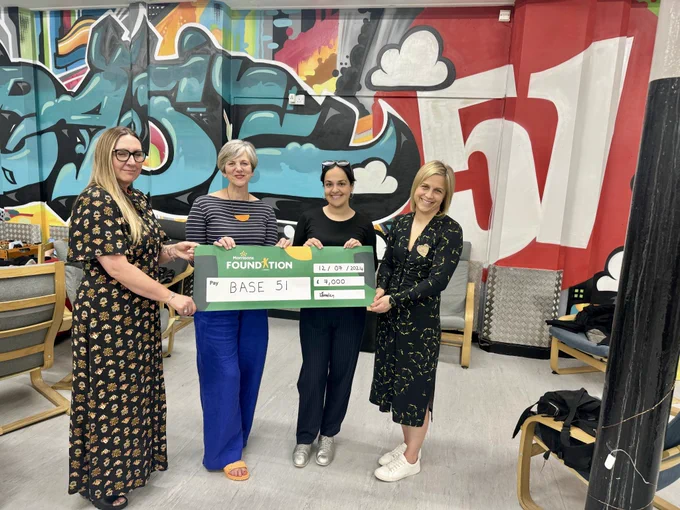 Nadia and Lilian standing with two members of the Base51 team, holding a cheque from the Morrisons Foundation