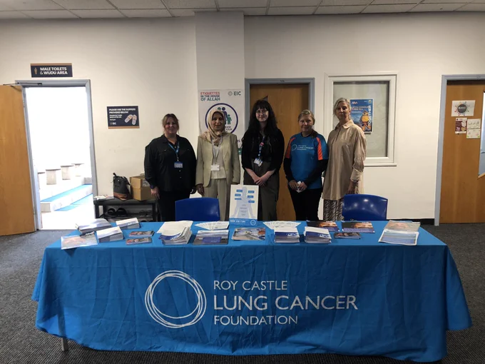 Staff stand behind a table with the Roy Castle Lung Cancer Foundation logo on.