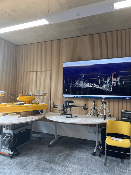 A stand at the FELS event. On one table there is a PicoCat and on the other is a drone and lidar scanner. The lidar scanner is connected to the screen, showing the people in the room.