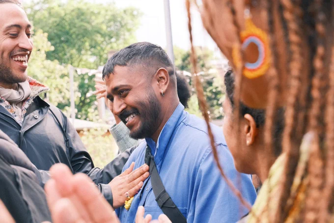 Kavian smiling, with other people around him. Another person is holding their hand on Kavian's heart.