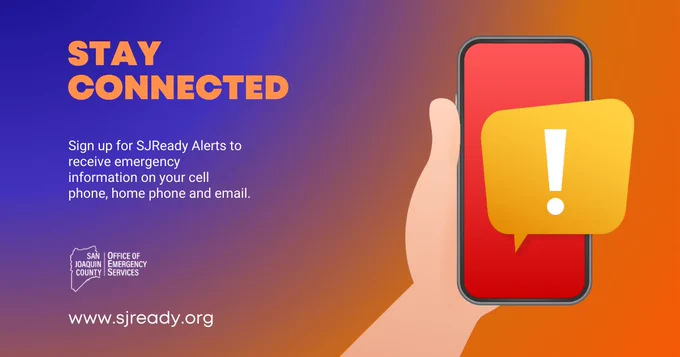 Hand holding a phone with a red screen and a yellow notification of an icon with an exclamation mark denoting emergency notification.