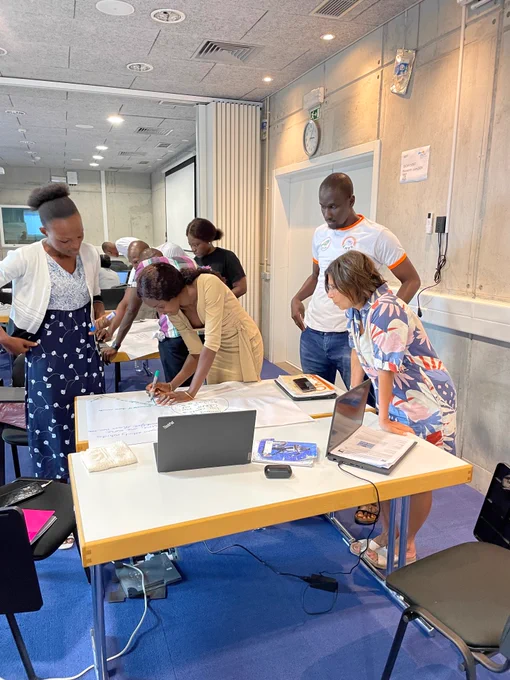 People in a room standing in front of a table with posters and laptops.