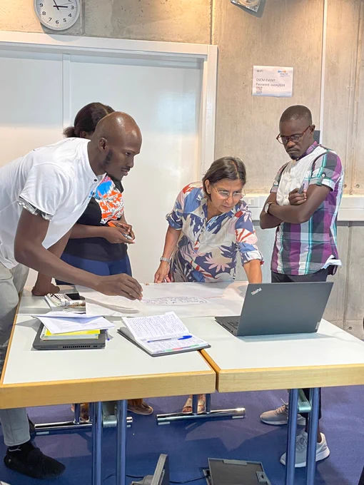 People in a room looking at a laptop and standing in front of a table with posters.