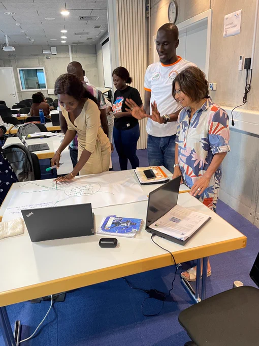 People in a room standing in front of a table with posters and laptops.