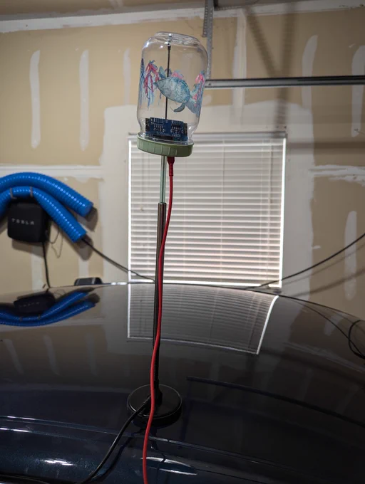 A @cod_segfault wardriver board in an inverted cheapo plastic cup, with the cup straw and a boba tea straw over a magnetic mount radio antenna. 