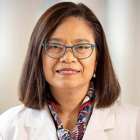 A professional portrait of an individual wearing glasses, a white lab coat, and a colorful scarf. The background is softly blurred, emphasizing the subject.