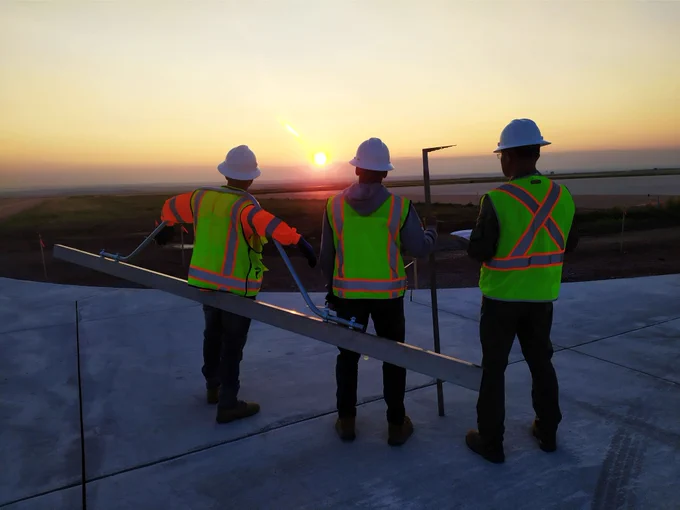 Three workers in construction hats watch a sunset 